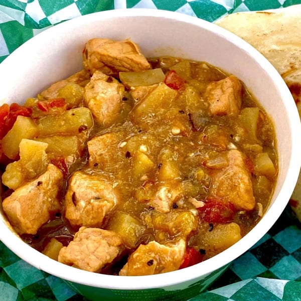 A bowl of The EVthing's American green chili with pork and potatoes, served with a tortilla.