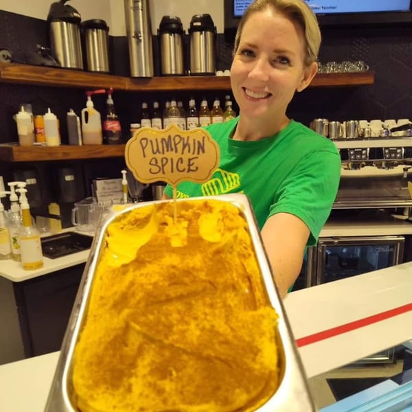 Smiling woman in green shirt holding a large tray of pumpkin spice ice cream at The EVthing.