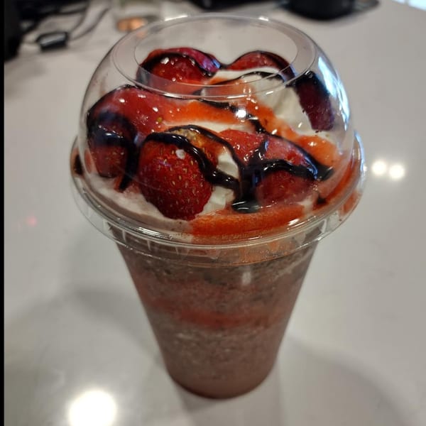 Chocolate milkshake with whipped cream, strawberries, and chocolate drizzle in a clear cup.
