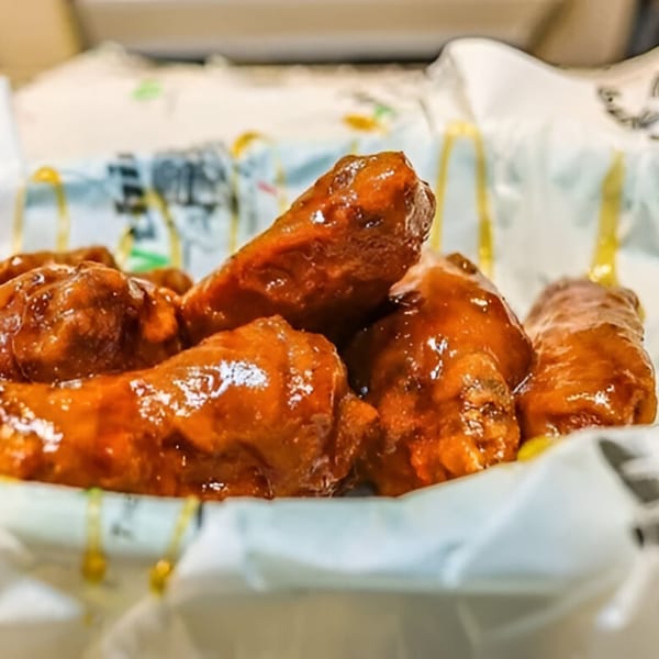 Close-up of several glossy, sauced chicken wings in a white paper-lined basket at The EVthing.