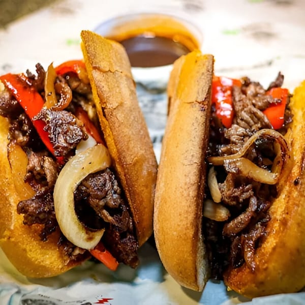 Two Philly cheesesteak sandwiches, cut in half, filled with steak, onions, and red peppers.