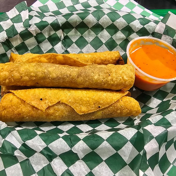 Crispy taquitos and a side of orange dipping sauce in a green and white checkered basket.
